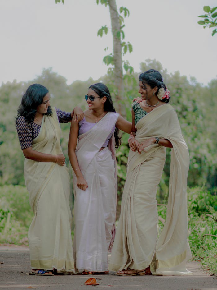 Three women enjoy a walk in the countryside wearing traditional sarees.