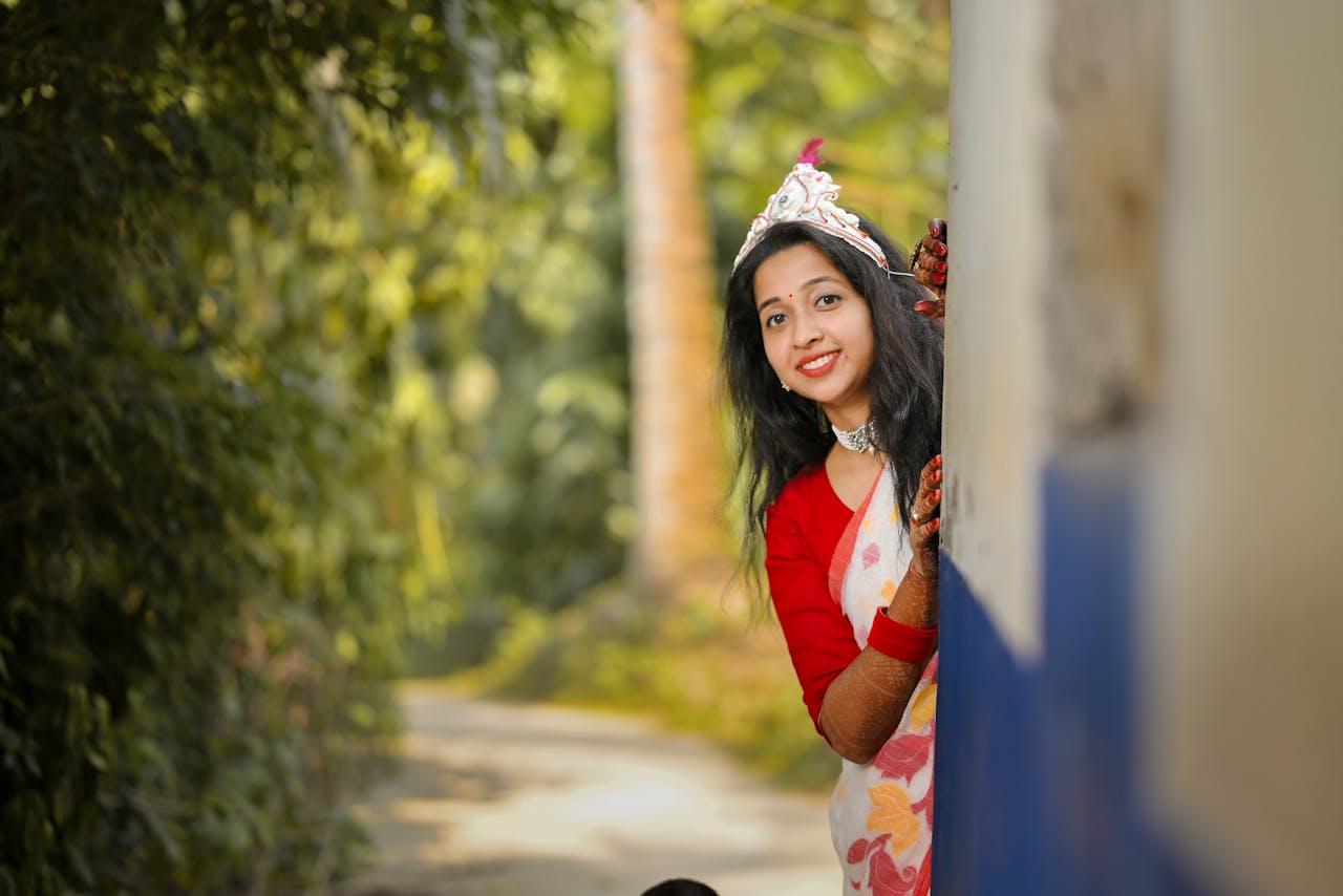 A traditional Bengali bride peeks playfully outdoors in a beautiful saree.
