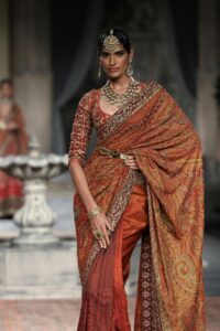 Model in ornate Indian saree showcases elegance during a high fashion runway event.