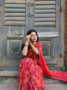 Portrait of a young woman in a red saree sitting by old architecture in Dhaka, Bangladesh.